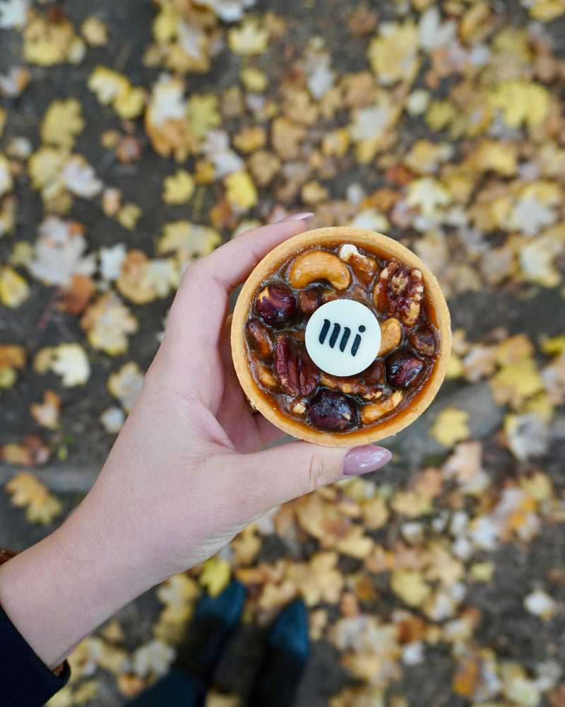 
                  
                    Load image into Gallery viewer, Hand holding a small round tart with a chocolate logo, filled with nuts and caramel on a fall background.
                  
                