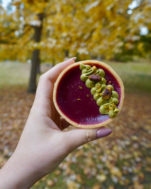 
                  
                    Load image into Gallery viewer, Hand holding a cranberry dessert tart with pistachio against a blurred autumn background
                  
                